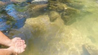 Şelaleden su tutan eller. Elleriyle su yakalayan genç adam. Derenin berrak suyu. Ailenle birlikte doğanın tadını çıkar, seyahat et, şelale turu yap.