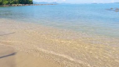 Güneşli bir günde kumlar kumlara vuruyor. Arka planda taş bariyer olan sahil. Tropik plaj, güzel plaj, sahilde deniz dalgaları.