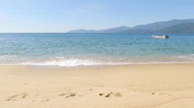 Güneşli bir günde deniz manzarası. Sahilde güneşli bir gün ve arka planda bir tekne. Deniz manzaralı. Yazın çok güzel bir yer. Okyanus dalgaları kumsala çarpıyor. Güzel manzaralı tropik plaj