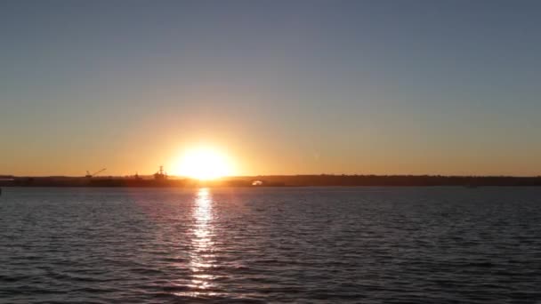 Sun setting over water in bay with silhouette of navy ship and reflection wide — Video