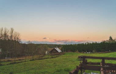 Şehir çiftliğinin üzerinde yükselen sarı ay ile dramatik akşam gökyüzü 