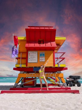 Miami Beach 'te ikonik bir cankurtaran evinin önünde sarı bikinili Brezilyalı bir kadın.