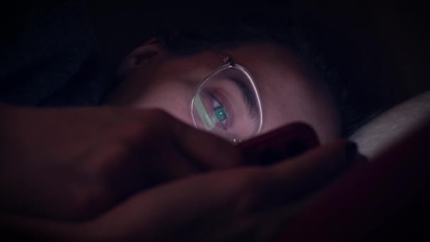Flicka bläddrar sociala medier på sin telefon medan hon ligger på sängen. Nattetid. närbild. — Stockvideo