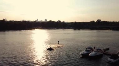 Genç adam rıhtımın yanında uçan bir kaykaya biniyor. Eğitim. Gün batımı. Drone görünümü.