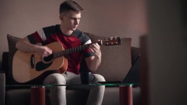Genç adam akustik gitar çalmayı öğreniyor. çevrimiçi öğrenme.