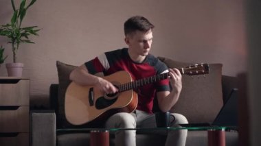 Genç adam evde online akustik gitar çalmayı öğreniyor.