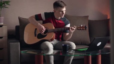 Genç adam evde online akustik gitar çalmayı öğreniyor.