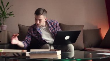 Mutlu genç adam pizza yer ve bilgisayarda çalışır. İç mekan. Uzaktan çalışma. dizüstü