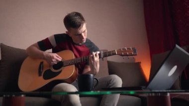 Neşeli genç adam akustik gitar çalmayı öğreniyor. uzak çevrimiçi ders.