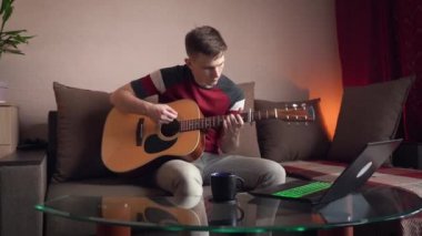 Genç adam evde online akustik gitar çalmayı öğreniyor.