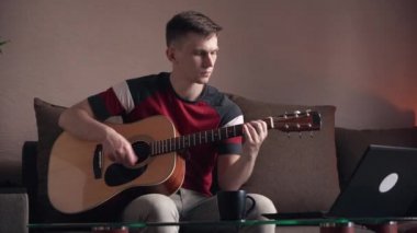 Genç adam evde online akustik gitar çalmayı öğreniyor.