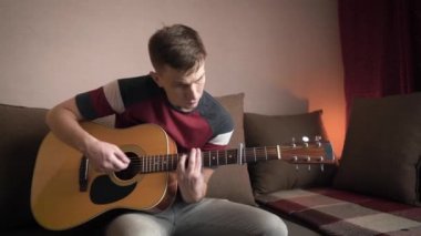 Genç adam akustik gitar çalmayı öğreniyor. çevrimiçi öğrenme.