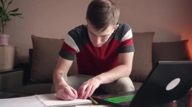 Genç adam evde bilgisayar kullanarak uzaktan öğrenme yapıyor. Koronavirüs izolasyonu.