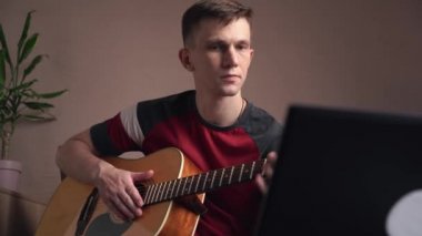 Genç adam akustik gitar çalmayı öğreniyor. çevrimiçi öğrenme.