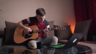Neşeli genç adam akustik gitar çalmayı öğreniyor. uzak çevrimiçi ders.