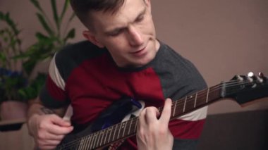 Genç adam dizüstü bilgisayarla elektronik gitar çalmayı öğreniyor. yakın plan