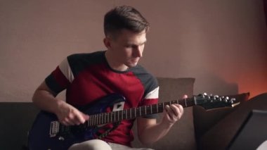 Genç adam dizüstü bilgisayarla elektronik gitar çalmayı öğreniyor. yakın plan
