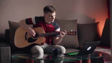 Genç adam akustik gitar çalmayı öğreniyor. çevrimiçi öğrenme.