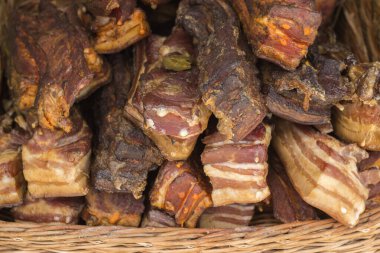 A stack of smoked bacon. Homemade food in a wicker basket on a market display.