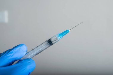 Doktorun parmakları mavi lastik eldivenlerle, parmaklarıyla aşı için hazır bir şırınga tutuyor. Aşı ve koruma araçları (covid-19, influenza) salgın hastalık ve sağlık kavramı