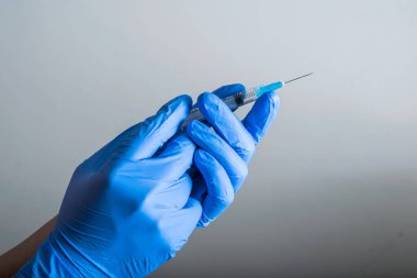 Doktorun ellerinde mavi lastik eldivenler, aşıya hazır bir şırınga, gri çözünmüş arka plan. Aşı ve koruma araçları (covid-19, influenza) salgın hastalık ve sağlık kavramı