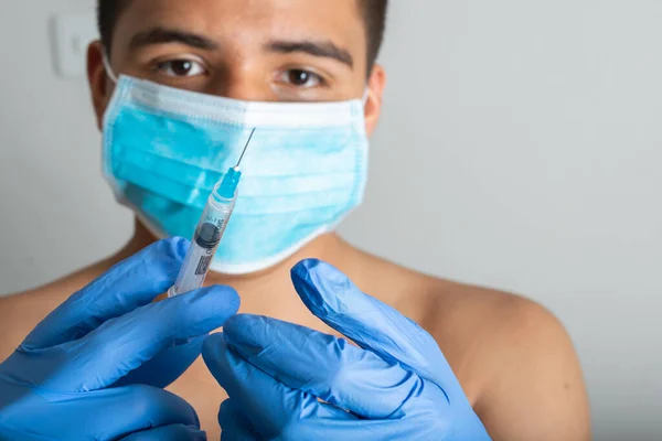 young latin man with surgical mask, shirtless, with a syringe preparing it for vaccination, Rembrandt illumination (45 light) vaccination instruments (covid 19, influenza) pandemic and health concept