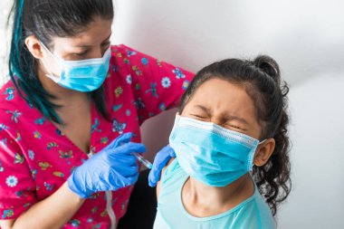 Çocukların hemşiresi kahverengi kızın koluna enjekte ediyor. Doktor kovid 19 aşısını enjekte ediyor. Kız gözlerini acıdan kapar ve gözlerini kaçırır, grip aşısı olur. tıbbi konsept, sağlık ve salgın hastalık.