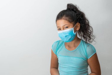 Küçük kız (8 yaşında) kolları aşağıda oturan kahverengi kız mavi cerrahi maskeli bir haber alıyor. Tıbbi, ilaç ve hijyenik konsept.