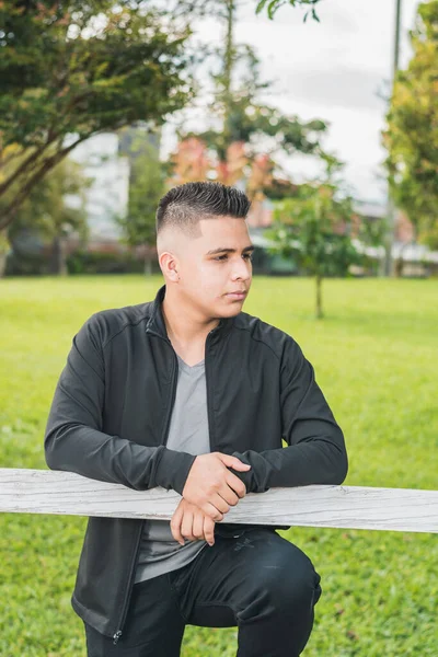 enterprising man standing by the white wooden fence with his hands on the fence, looking to the left thinking about his future young college student in a black suit. vertical photograph
