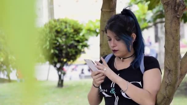美しい深刻な若い女性 青い髪の女子大生が公園でソーシャルメディアを見ている 公園で携帯電話を見てた コミュニケーション 教育の概念 — ストック動画