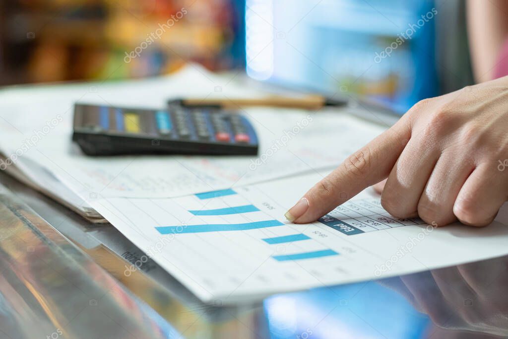 a latina girl's hand is pointing to the sales statistics bars. in the background a pencil and a small calculator on top of a notebook for notes. business and sales concept