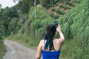 Kolombiya 'da ekolojik bir patikada yürüyüş yapan genç Latin kız cep telefonuyla doğayı belgeliyor. Kadın nüfuzlu kişi sosyal ağları için içeriği kaydediyor. yürüyüş kavramı.