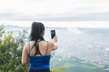 Kız nüfuzlu kişi, yürüyüş yaparken sosyal ağları için içerik yaratıyor. Teknoloji konsepti. Soğuk bir günde yürüyüş yapan Latin bir kadın güzel manzaranın fotoğraflarını çekiyor..