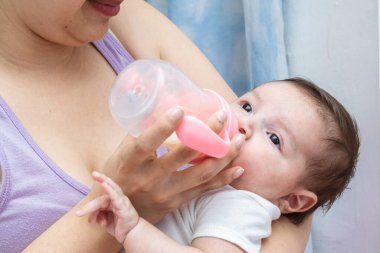 Güzel Latin bir bebek, gözleri açık, annesinin açlığını dindirmek için verdiği şişeyi alıyor. Bebek uykulu bir yüzle uykuya dalmak üzere..