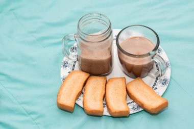 İki kişilik kahvaltı, tek bir tabakta kızarmış ekmek ve açık mavi arka planda çikolatalı iki cam bardak ile servis edilir. Bir çift için hafif atıştırmalık. Latin kahvaltısı