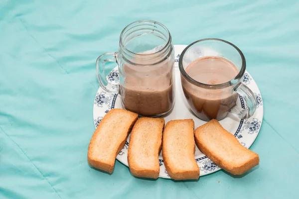 İki kişilik kahvaltı, tek bir tabakta kızarmış ekmek ve açık mavi arka planda çikolatalı iki cam bardak ile servis edilir. Bir çift için hafif atıştırmalık. Latin kahvaltısı