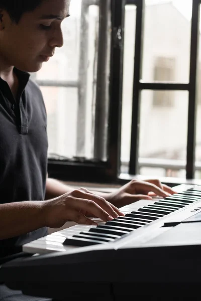 very concentrated latin guy playing electric piano or synthesizer at home. young man studying music production through internet. musical and recreational concept.
