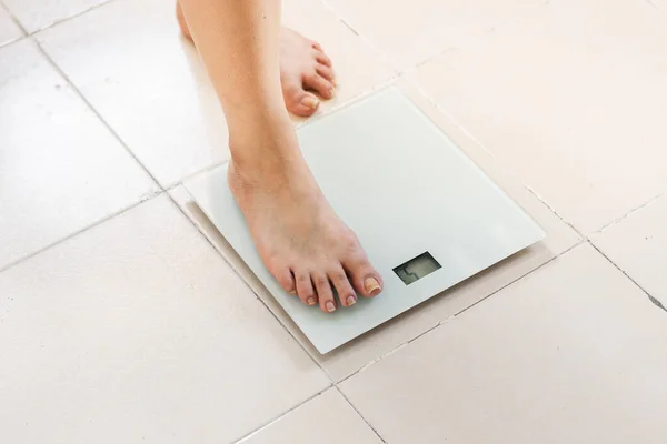 detail view of the feet of a latina woman, with one foot placed on the scale, measuring her weight to have a correct state of health and to have a good diet. white digital glass scale