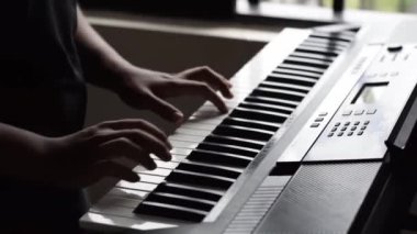 Genç bir Latin öğrencinin ellerinin yakın çekimi, sentezleyicisiyle piyano notaları çalışıyor. Kahverengi tenli çocuk performansı için şarkıyı prova ediyor. Müzik disiplini kavramı.