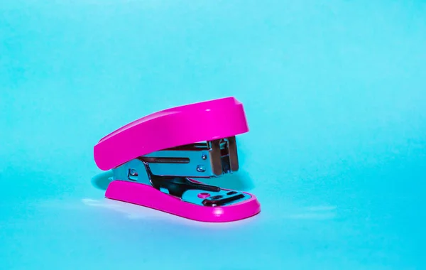 small pink stapler for paper, on a blue background. item used for office work and document archiving. practical portable stapler.