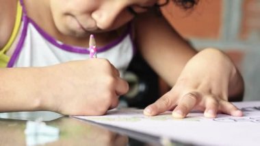 Kahverengi tenli Latin bir kızın, ödevini yeşil kalemle boyaması, düşük gelirli Kolombiyalı öğrencinin çizimlerine konsantre olması. yoksulluk ve yoksulluğun üstesinden gelme kavramı