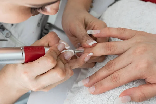 close-up detail of a manicurist\'s hands polishing nails made of polygel with an electric nail buffer with a conical or bullet-shaped bit for higher pressure. pointed bit for filing