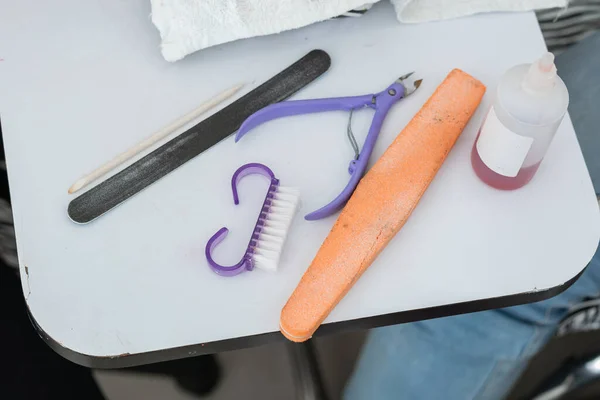 basic elements for performing a basic manicure on a table suitable for the correct positioning and work of the hands. wooden stick, nail file, cuticle nipper, nail brush and liquid cuticle remover.