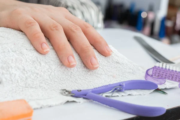 detail of a latina girl\'s hand, placed on the resting pad waiting to start a manicure, surrounded by manicure elements such as a cuticle nipper, a nail brush and a nail feeder.