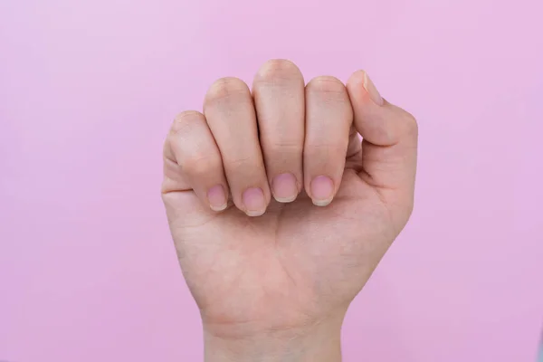 hand of a latin woman showing her nails in a closed hand pose, in the background a pink cardboard, semi arranged nails ready for the realization of a nail painting and decoration.