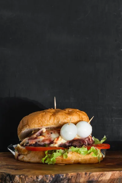 close-up of a Colombian hamburger, with a black background with space to copy text. bread, lettuce, tomato, hamburger meat, Mozzarella cheese, bacon, quail egg and pink sauce, on a wooden board.