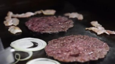 detail shot of two hamburger meats being grilled on a grill, along with bacon and onion slices. ingredients for preparing fast food in colombia. junk food concept.
