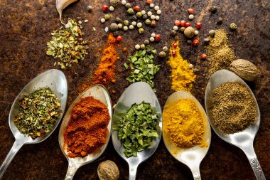 Paslı arka planda eski metal kaşıklara saçılmış farklı mutfak baharatları seti. Üst Manzara. Yemek pişirme mevsimleri