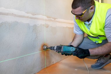 Gözlüklü usta bir elektrikçi, elektrik prizi kurmak için duvarda bir delik açar ve kapatır.