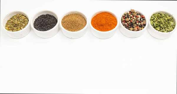 Different kinds of spices of different colors scattered in ceramic bowls isolated on white background, place for text